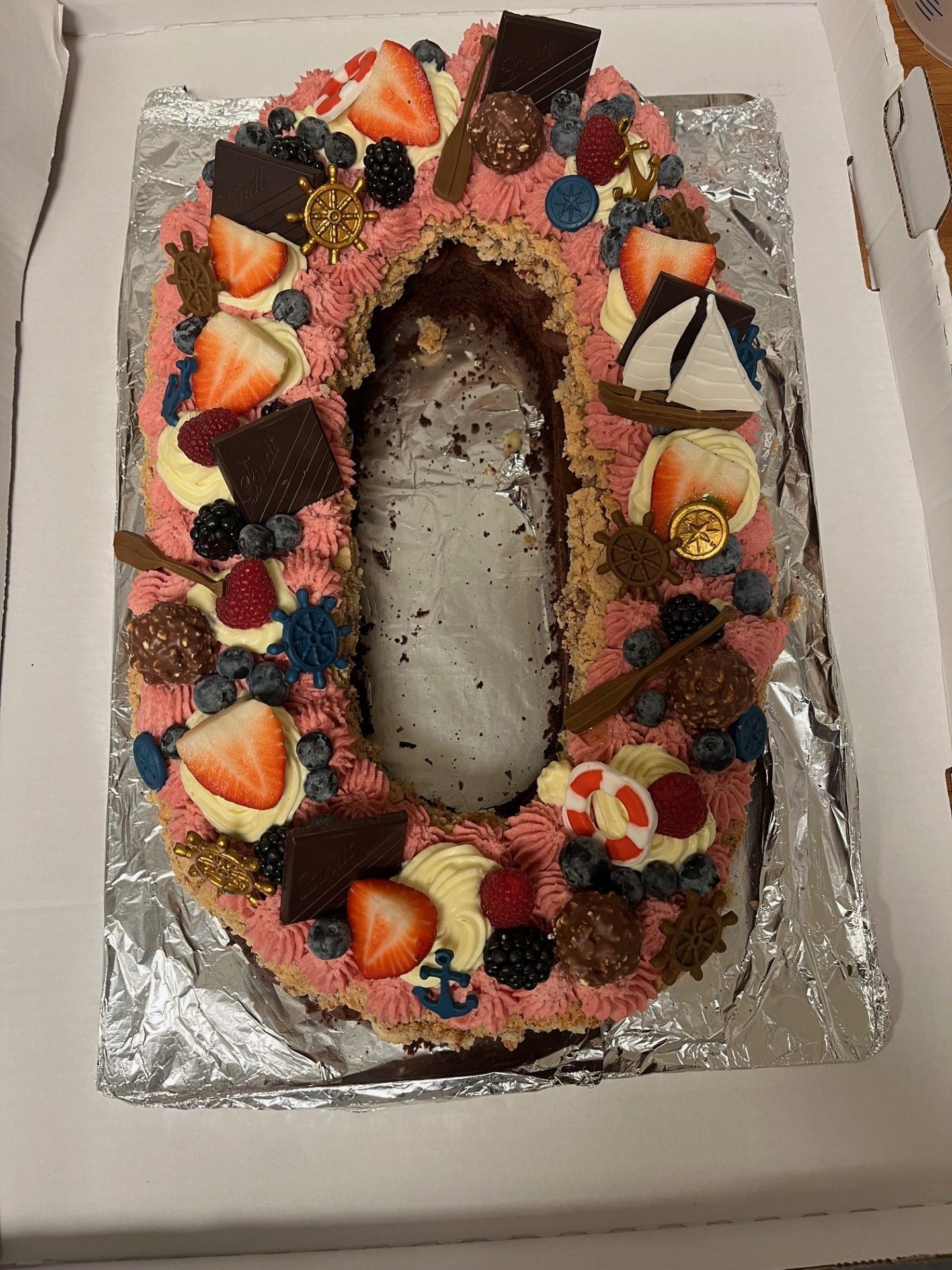 Bådformet kage dekoreret med lyserød frosting, jordbær, blåbær og chokoladestykker på et sølvfad.