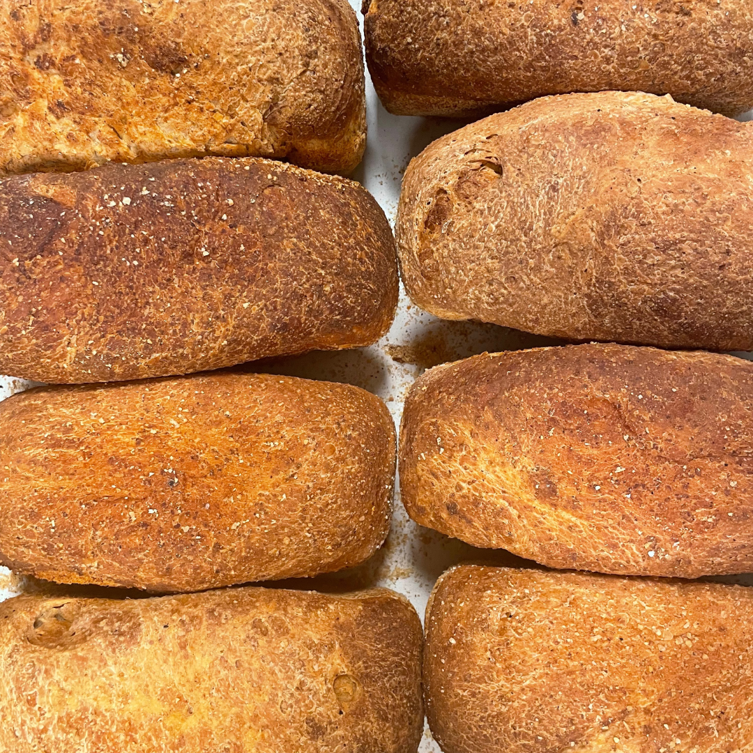 Seks gyldenbrune brød stablet tæt sammen på en hvid overflade