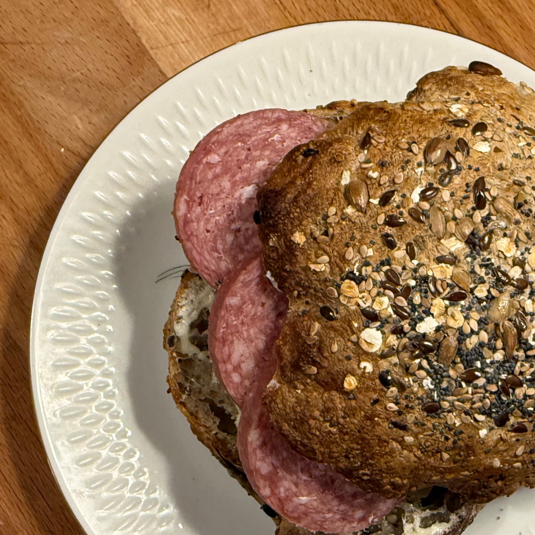 Åben sandwich med skiver af salami på rustikt brød med kerner på en hvid tallerken