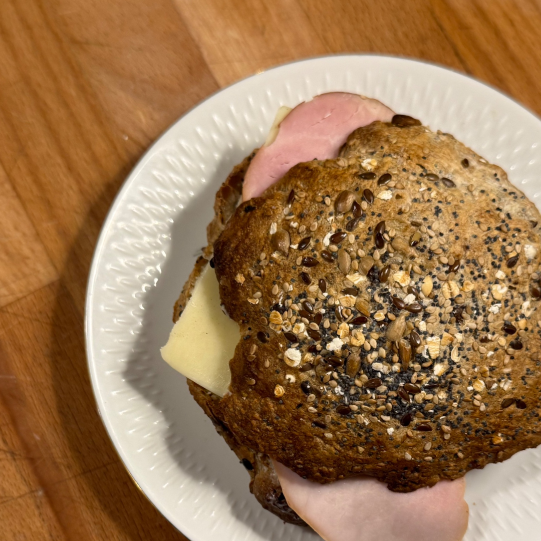Flerkornssandwichbolle med skinke og ost på en hvid tallerken