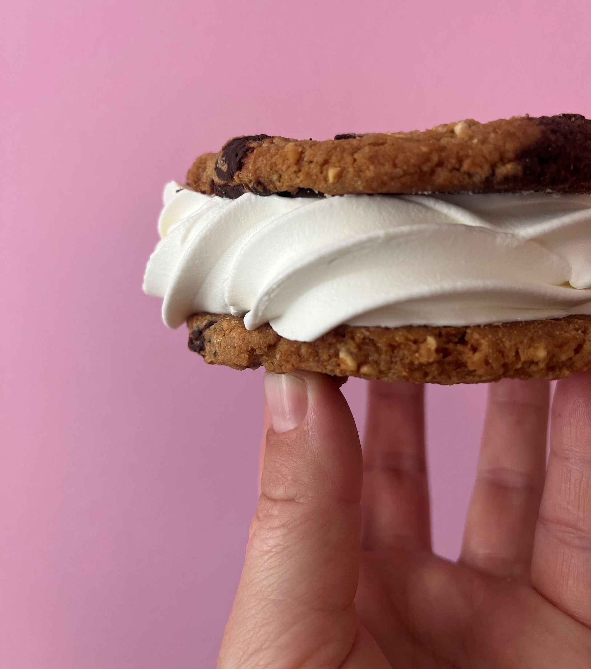 Hånd, der holder en cookie-is-sandwich mod en lyserød baggrund.