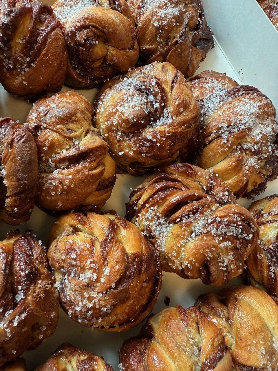 Nærbillede af gyldenbrune kanelboller, hvirvlet og toppet med granuleret sukker, i en hvid æske.
