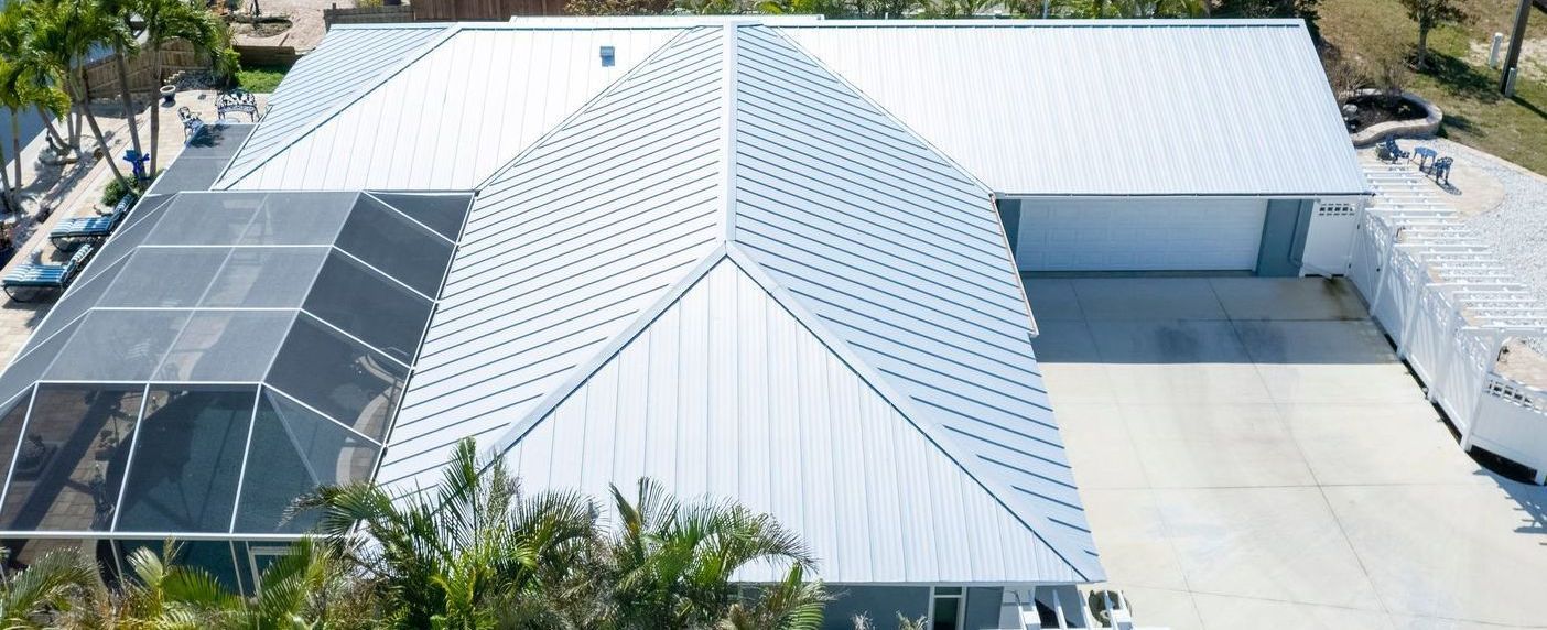 Aerial view of a modern white roofed house with a pool cage and a driveway.