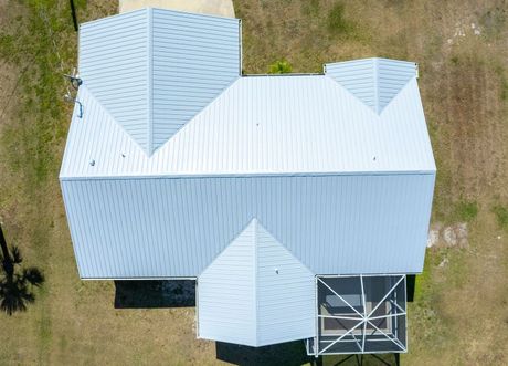 Overhead view of a light blue roof with multiple gables, house set in a grassy yard.