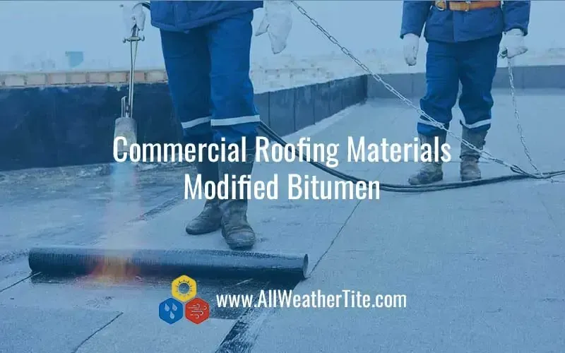 Two workers installing modified bitumen roofing on a flat roof with a blow torch.