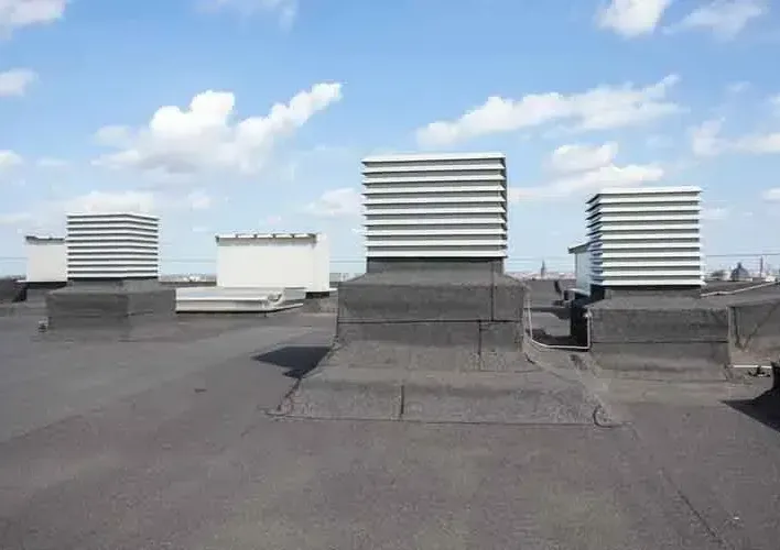 Flat roof with three square air vents and a cloudy blue sky.