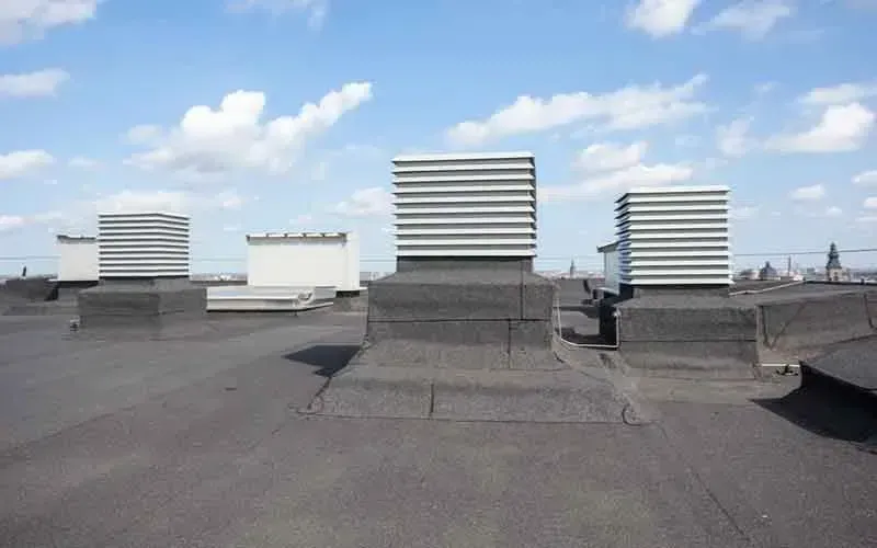 Flat, dark rooftop with ventilation units against a blue sky.