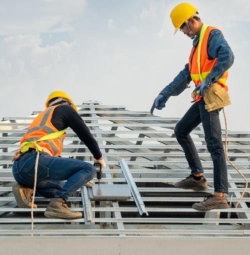 Two construction workers on a rooftop wearing hard hats and vests. One points at a metal frame.