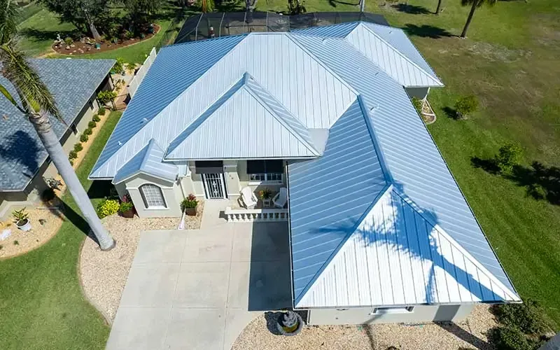 Silver metal roof on a light-colored house with a driveway and green lawn.