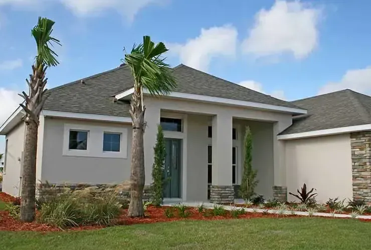 Modern, light-colored house with stone accents, palm trees, and green lawn against a blue sky.
