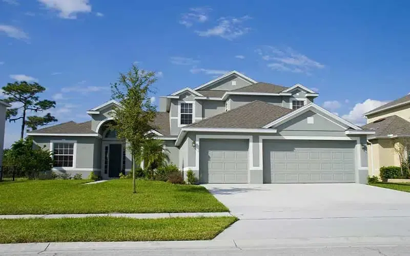 Two-story gray house with a green lawn, driveway, and blue sky.