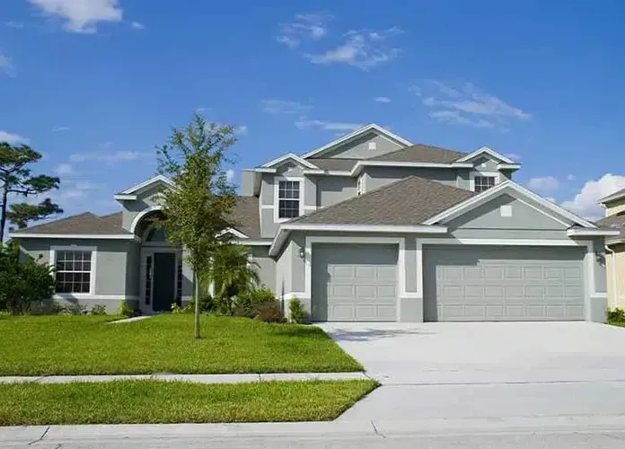 Two-story gray house with a two-car garage, green lawn, and blue sky.