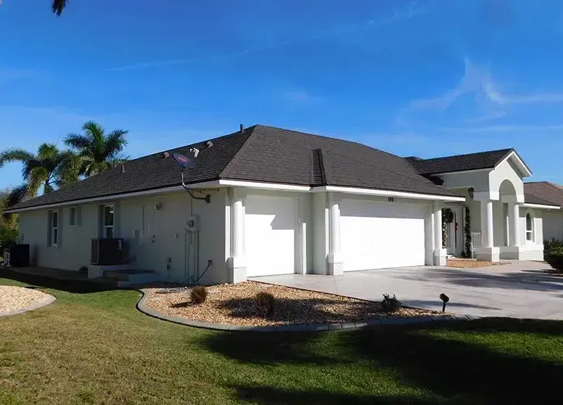 A stucco house with a black roof and a white garage door under a blue sky.