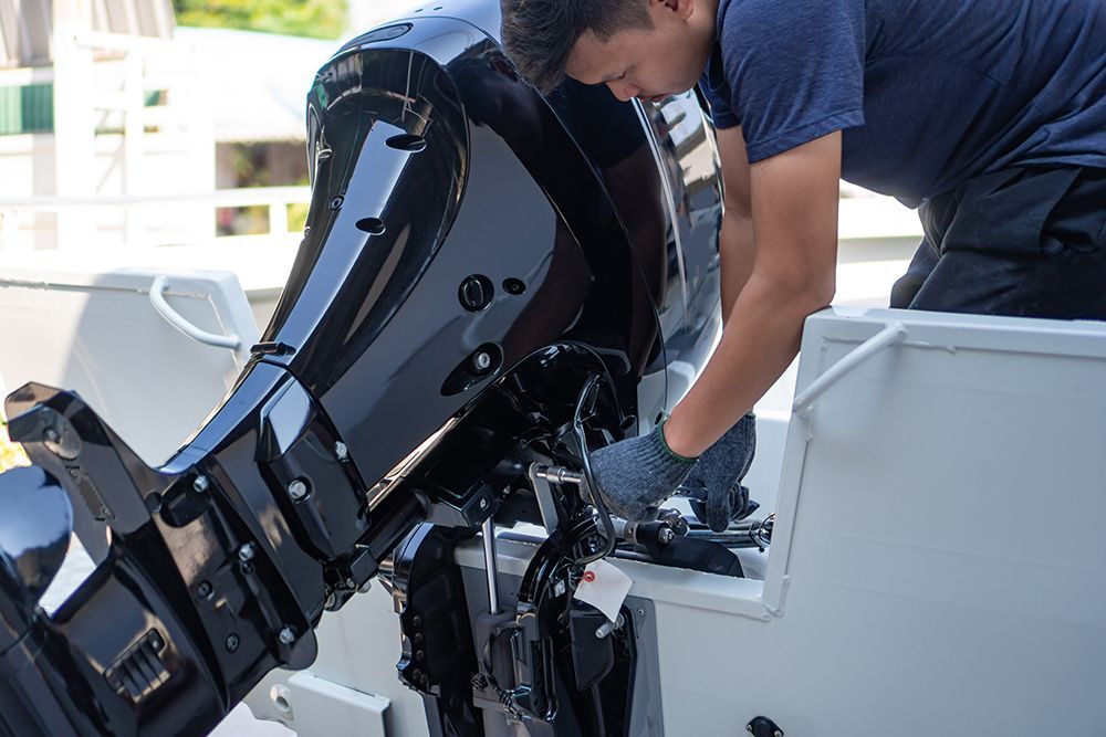 Man in blue shirt working on a boat motor, outdoors, in sunlight.