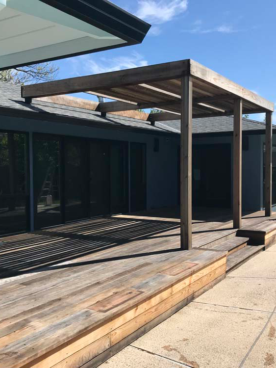 A wooden deck with a pergola in front of a house.