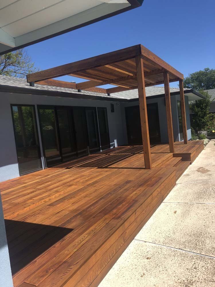 A wooden deck with a pergola over it in front of a house.
