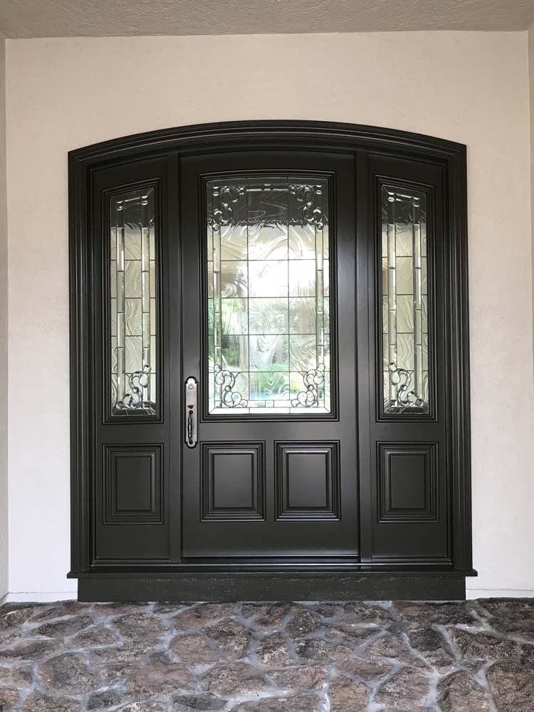 A black door with stained glass is in a room with a stone floor.