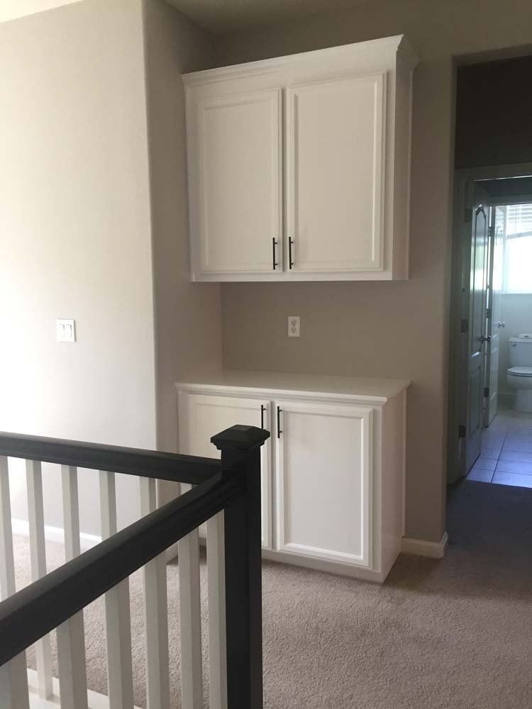 A hallway with white cabinets and a black railing leading to a bathroom.