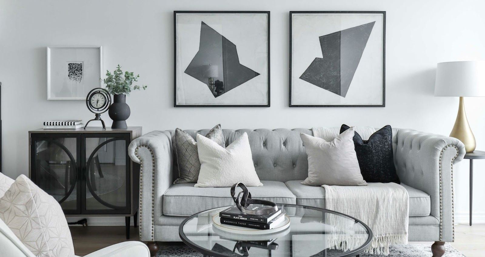 A living room with a couch , chair , coffee table and two paintings on the wall.