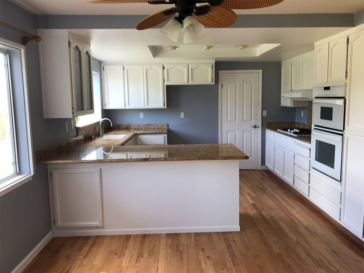 An empty kitchen with white cabinets and a ceiling fan