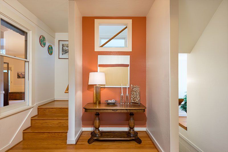 A hallway with a table , mirror , lamp and stairs.