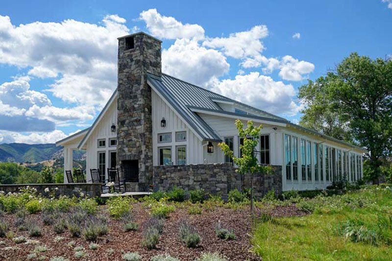A large white house with a stone chimney is sitting on top of a grassy hill.
