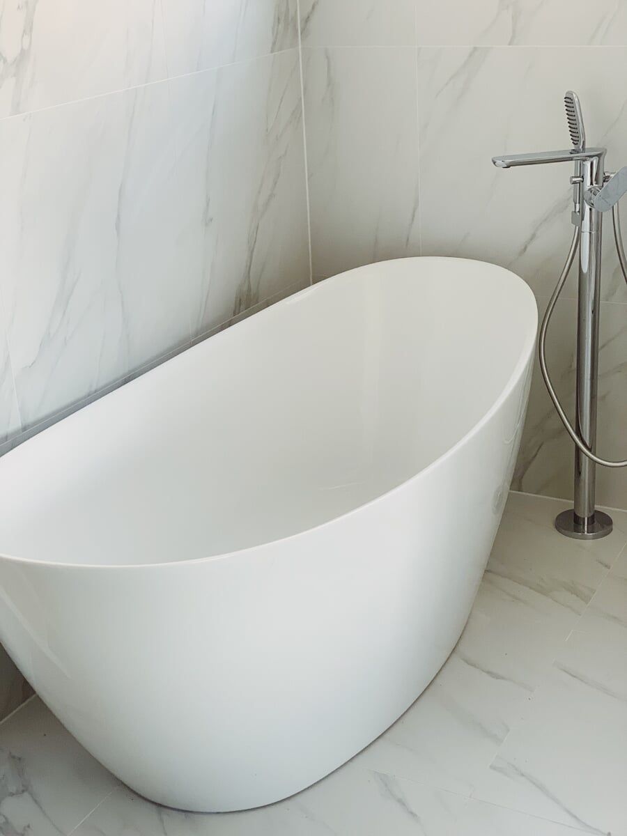 A White Bathtub is Sitting in a Bathroom next to a Faucet — Illawarra Bathrooms in Wollongong, NSW	