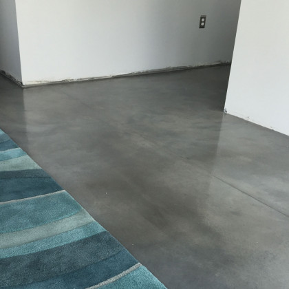 Polished gray concrete floor in a room with white walls; blue rug in corner.