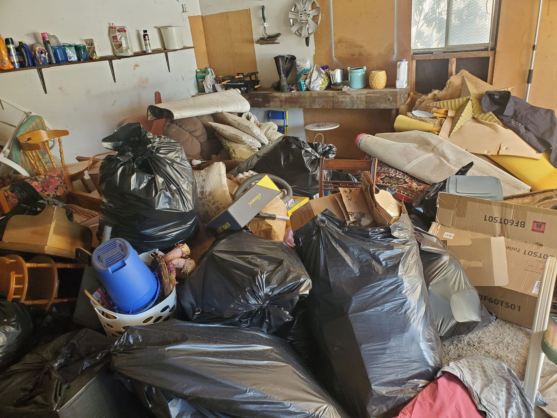 A cluttered room with black trash bags, boxes, and miscellaneous items piled high.