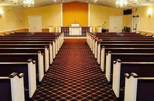 Empty church sanctuary with rows of pews facing a pulpit on a red carpet aisle