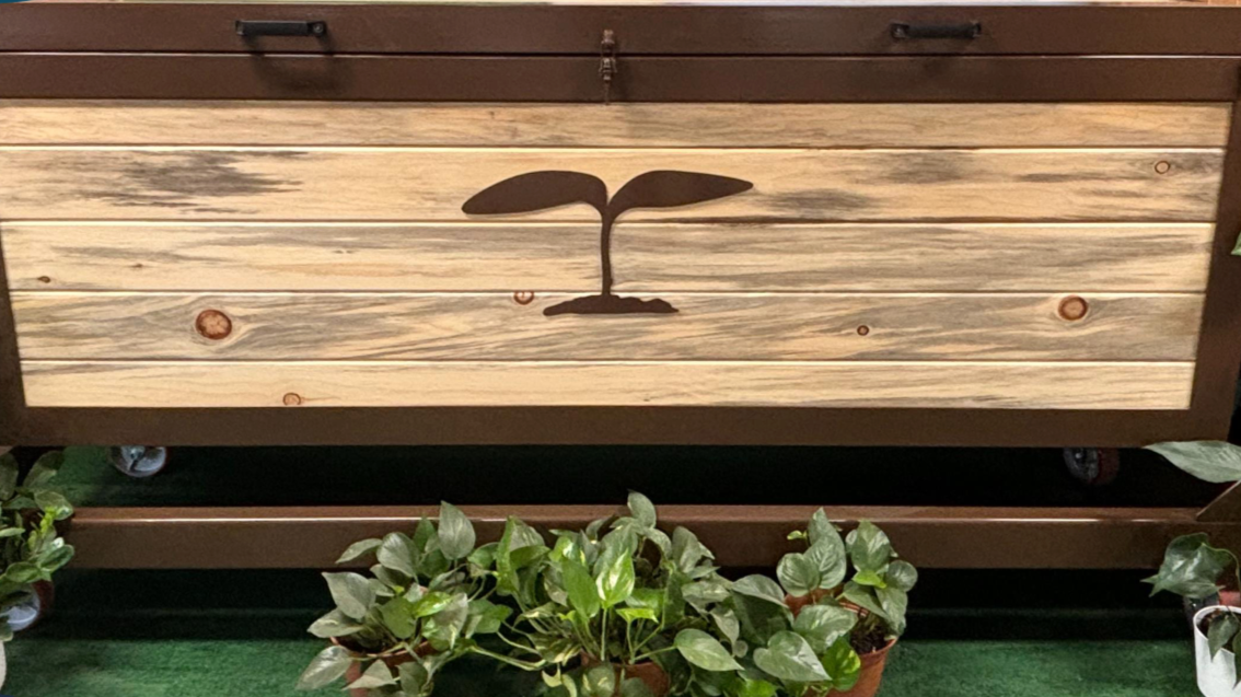 Wooden planter box with a sprouting plant icon, above a bed of green plants.