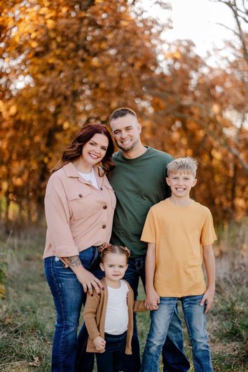 A family is posing for a picture in a field with trees in the background.