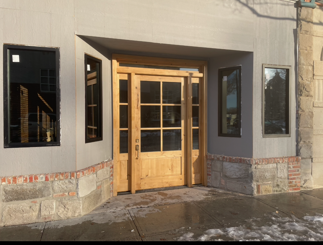 A building with a wooden door and windows on the sidewalk