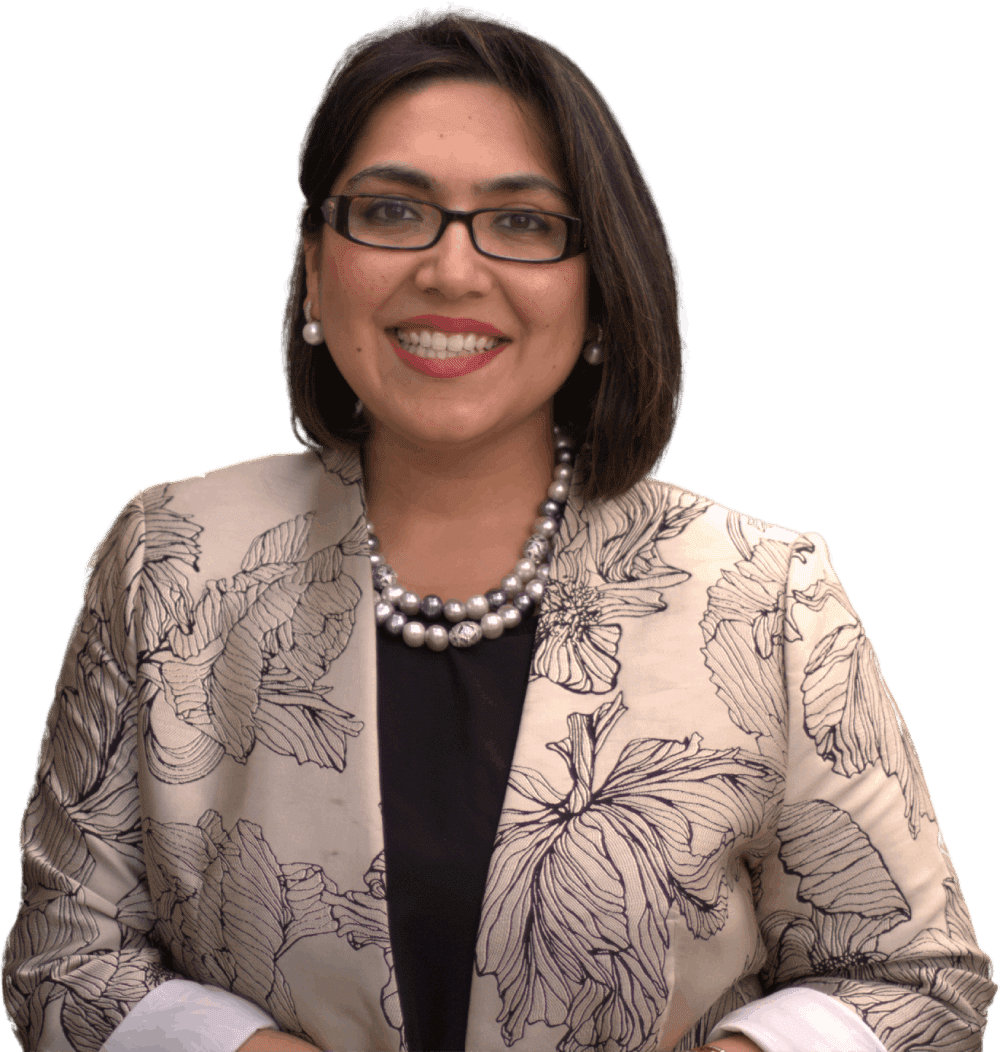 Smiling woman in glasses wearing a patterned blazer and pearl necklace against a white background