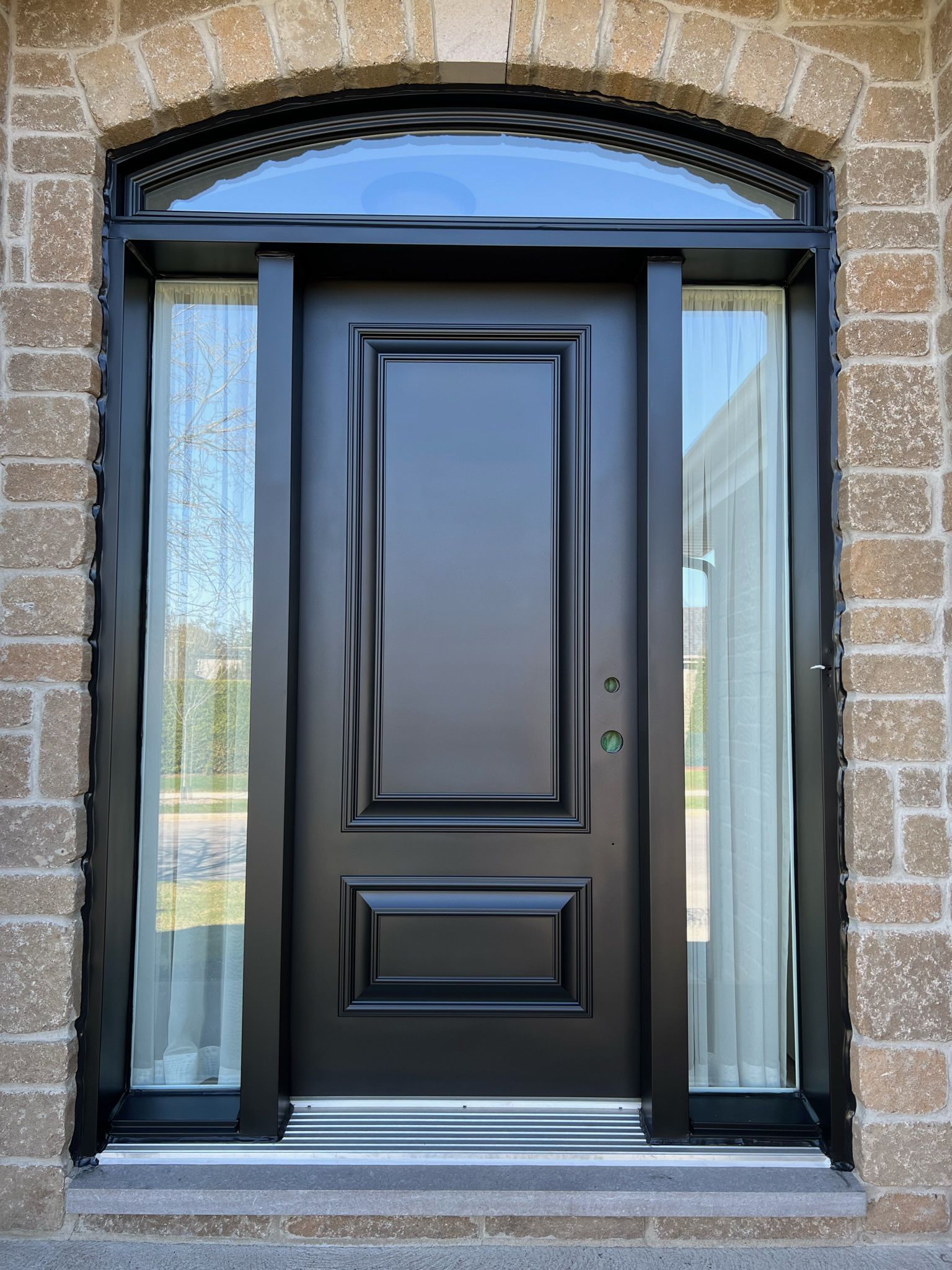 A black front door with a window in a brick building.