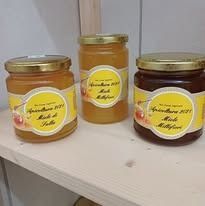 Tre barattoli di miele in vetro con coperchi dorati ed etichette gialle, su uno scaffale di legno.