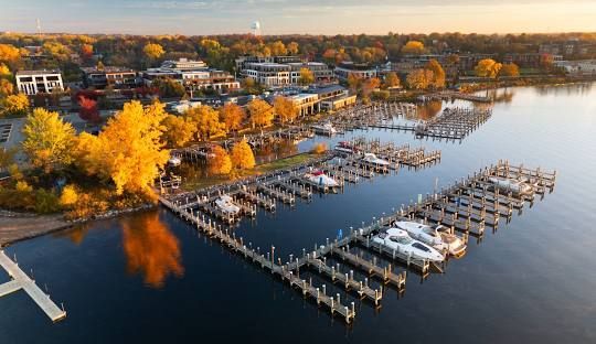 Marina on a lake with docks, boats, and fall foliage in a waterfront town at sunset.