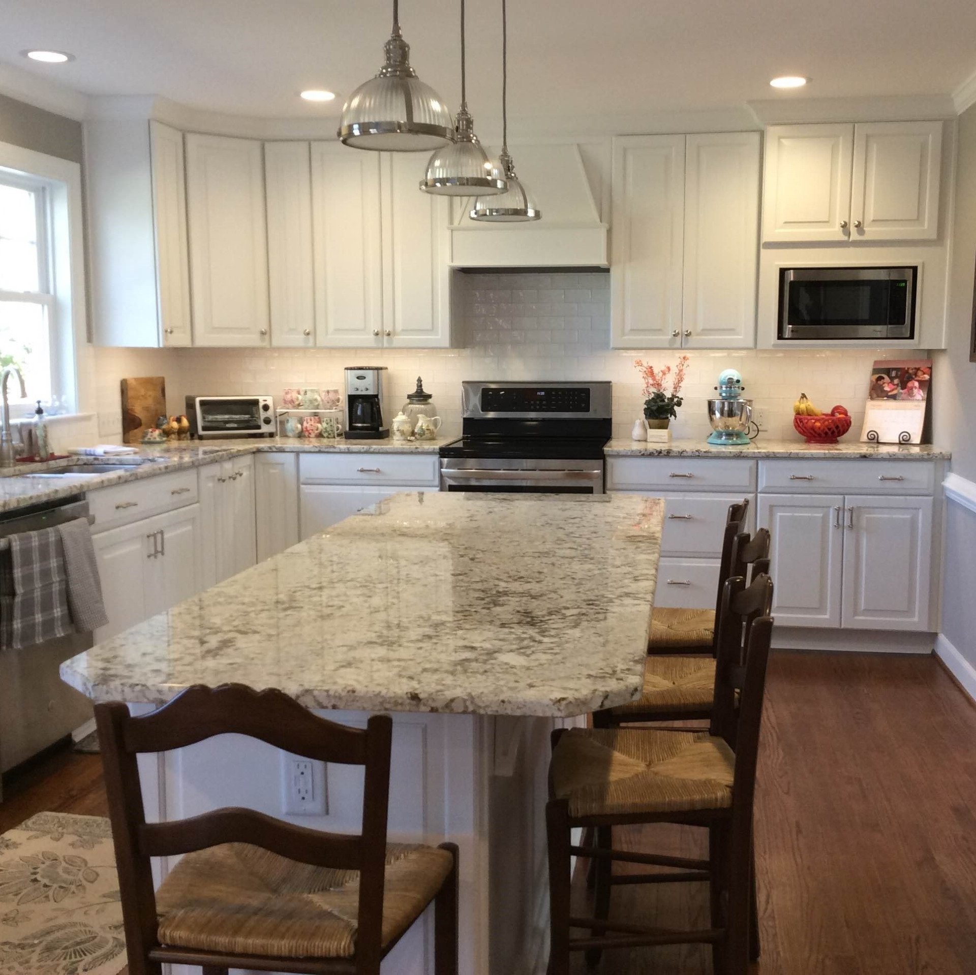 Bright kitchen with white cabinets, granite island, stainless appliances, and wood chairs around the counter