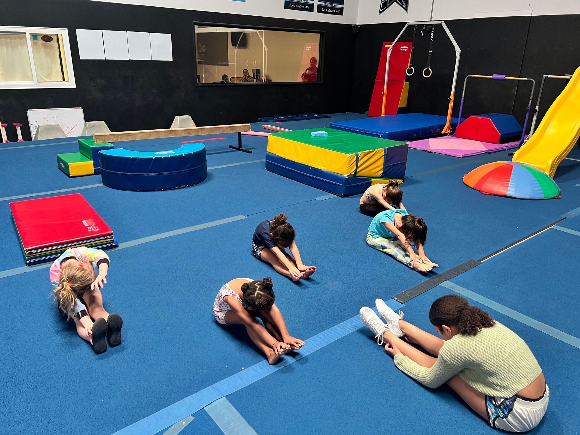 A group of children are stretching on the floor of a gym.