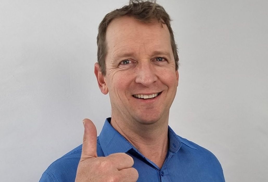 A man in a blue shirt is giving a thumbs up.