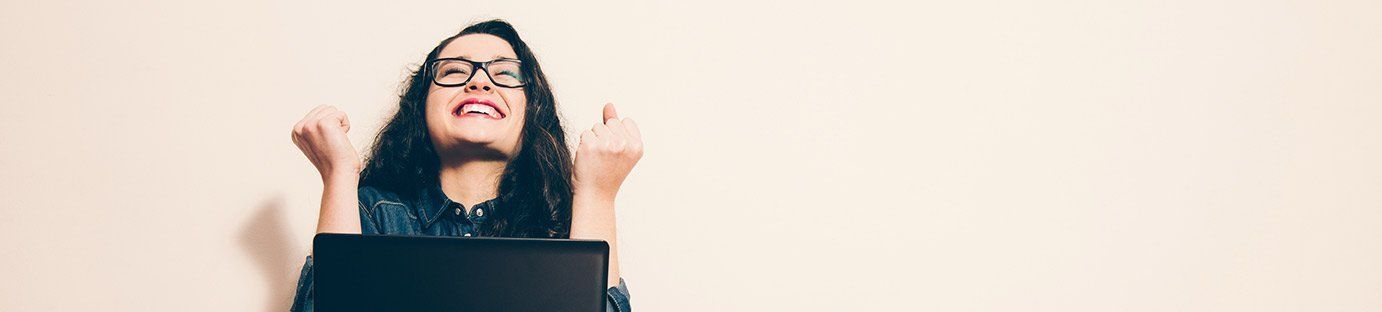 A woman is sitting in front of a laptop computer with her hands in the air.