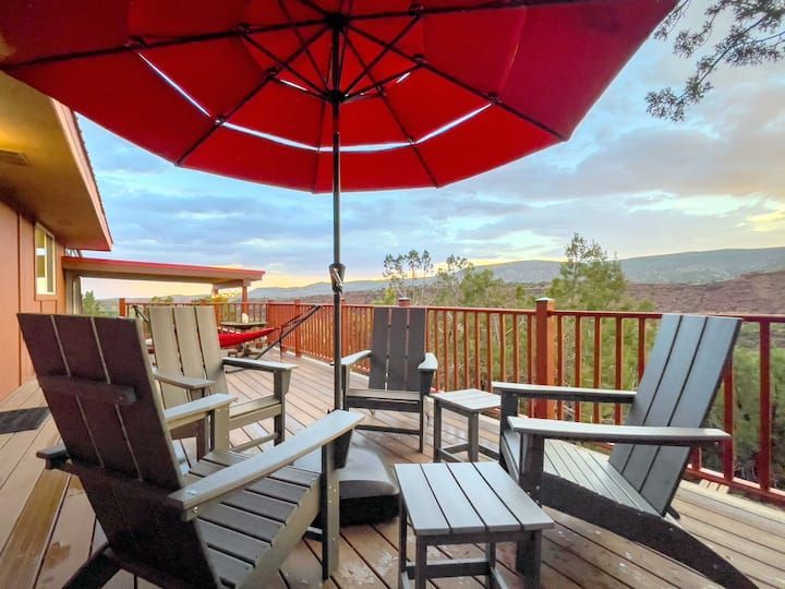 Patio with red umbrella, wooden chairs, and mountain view beyond a deck railing