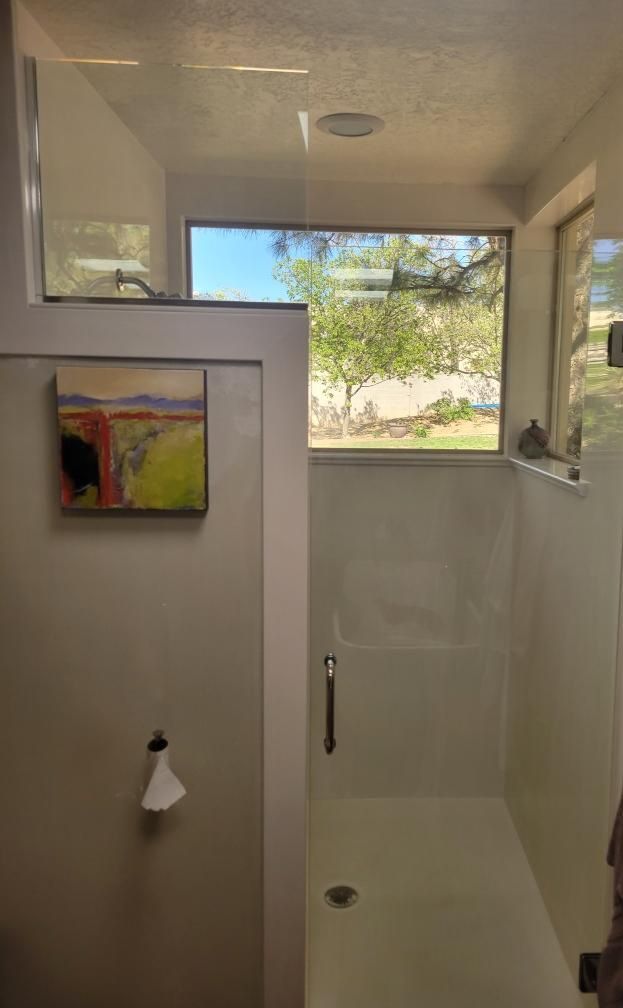 Small bathroom with a white shower stall, frosted window, and a colorful wall painting.