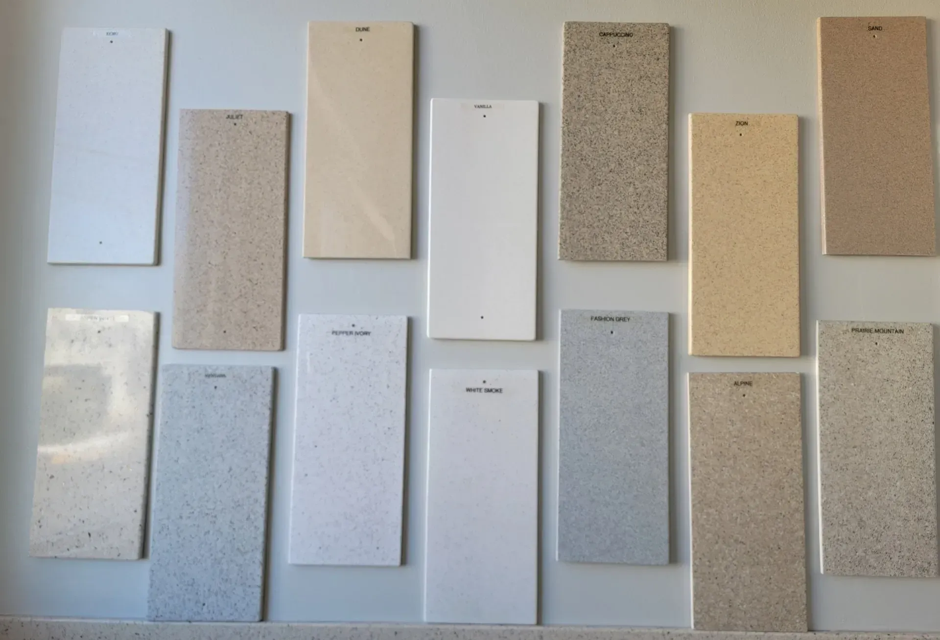 Array of beige and white rectangular sample panels with speckled textures, displayed on a wall.