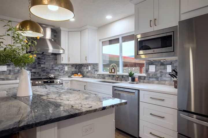 Modern kitchen with white cabinets, gray marble countertops, stainless appliances, and pendant lights