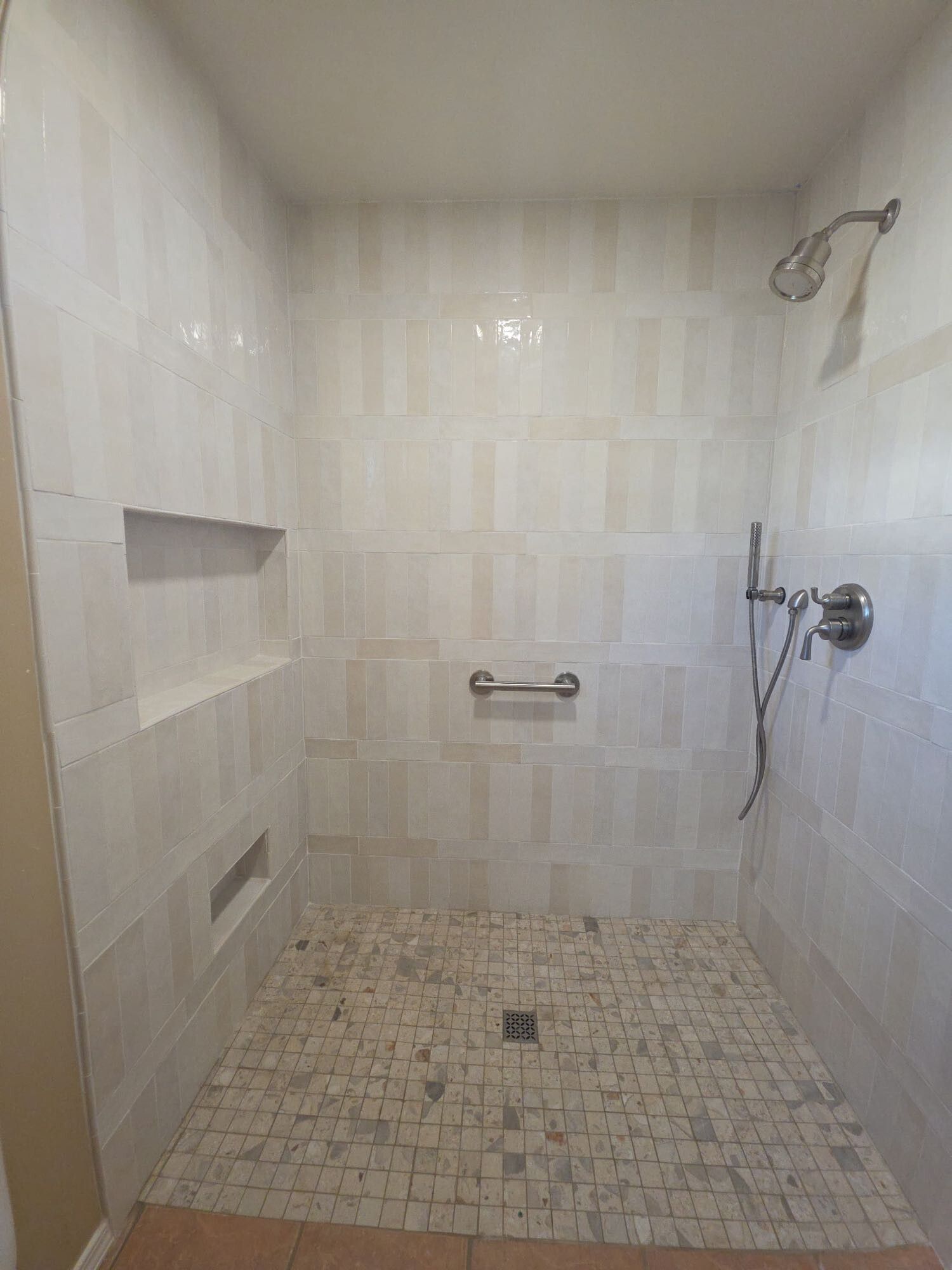 Empty tiled walk-in shower with built-in niches and a handheld showerhead on the right.