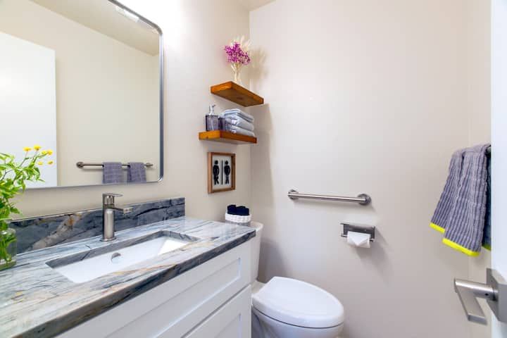 Modern white bathroom with vanity, mirror, toilet, towel rack, and wall shelves