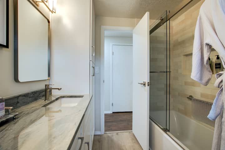 Modern bathroom with double vanity, large mirror, glass shower, and open door to hallway