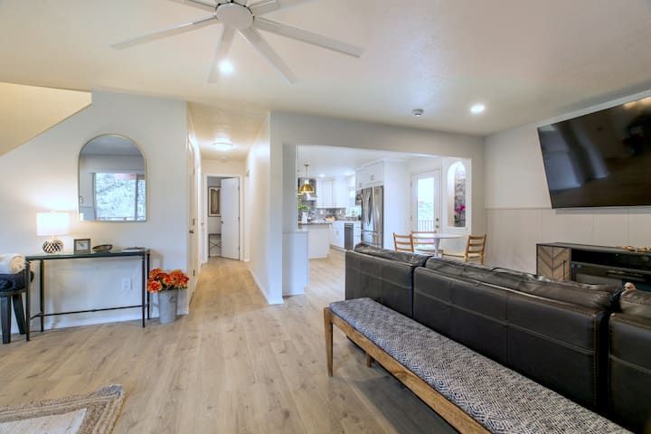 Bright modern living room with gray sectional, wall TV, fireplace, and open hallway to kitchen