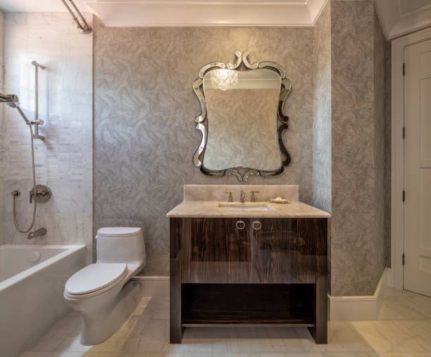Elegant modern bathroom with marble shower, toilet, vanity and ornate mirror over sink cabinet room.
